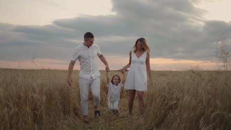 Happy-smiling-family-holding-hands-walking-through-golden-field-at-sunset.-Happy-family-walking-on-meadow-and-playing.